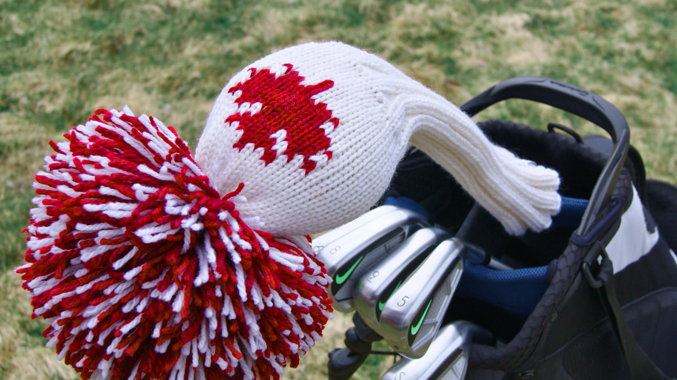 a white knit golf club cover with a red maple leaf and a red and white pompom