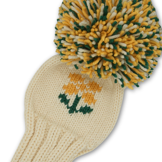 A knitted driver cover in off white with a yellow flower motif and large pompom