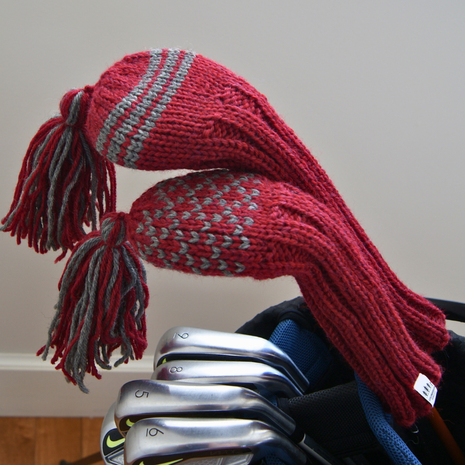 Red knitted golf club cover with tassels on a golf club set against a neutral background