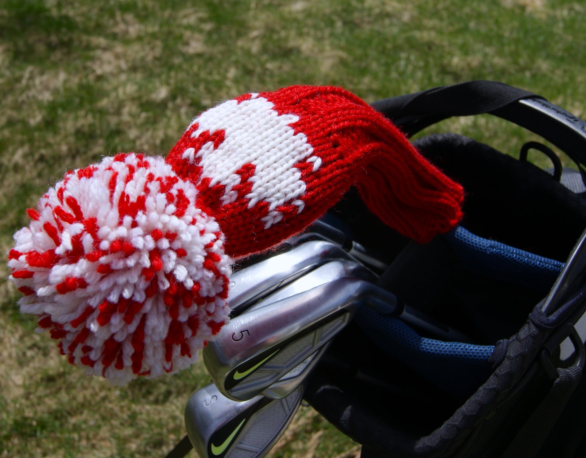 Golf club cover with red and white knitted maple leaf design on a grass background